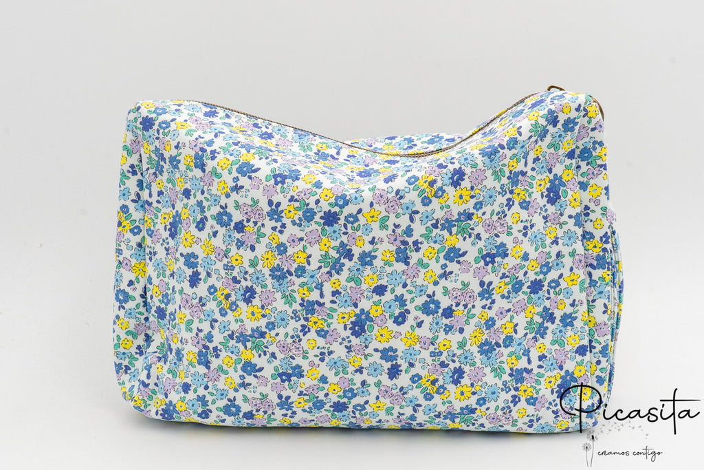 Neceser de tela con flores azules y amarillas visto de frente sobre fondo neutro.