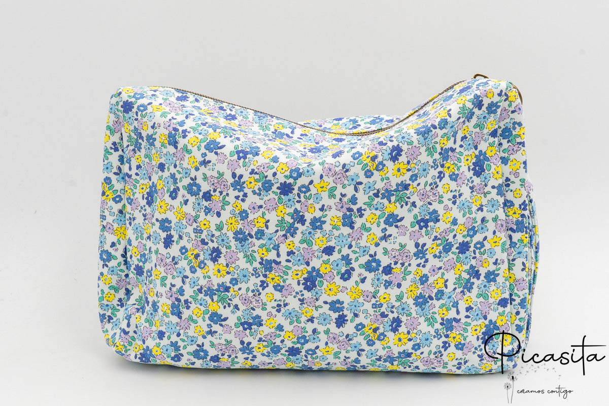 Neceser de tela con flores azules y amarillas visto de frente sobre fondo neutro.
