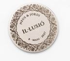 Moneda nupcial grabada con corona de rosas y nombres de los novios en catalán.