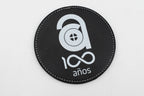 Round black coaster with a white centenary logo.