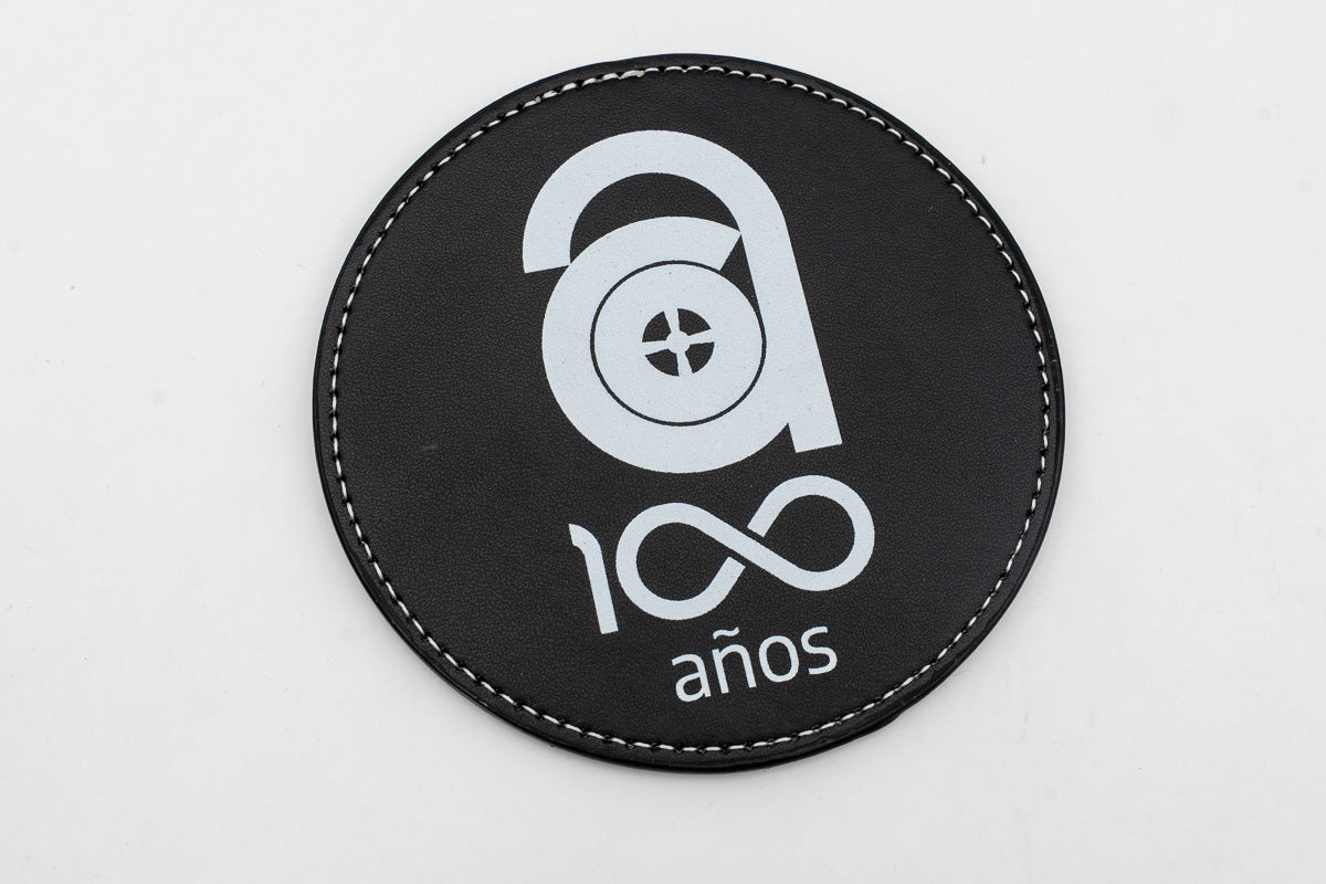 Round black coaster with a white centenary logo.