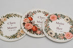 Three round white coasters with colourful flowers and couples’ names.