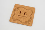 Square cork coaster with a decorative frame and initials J and C.