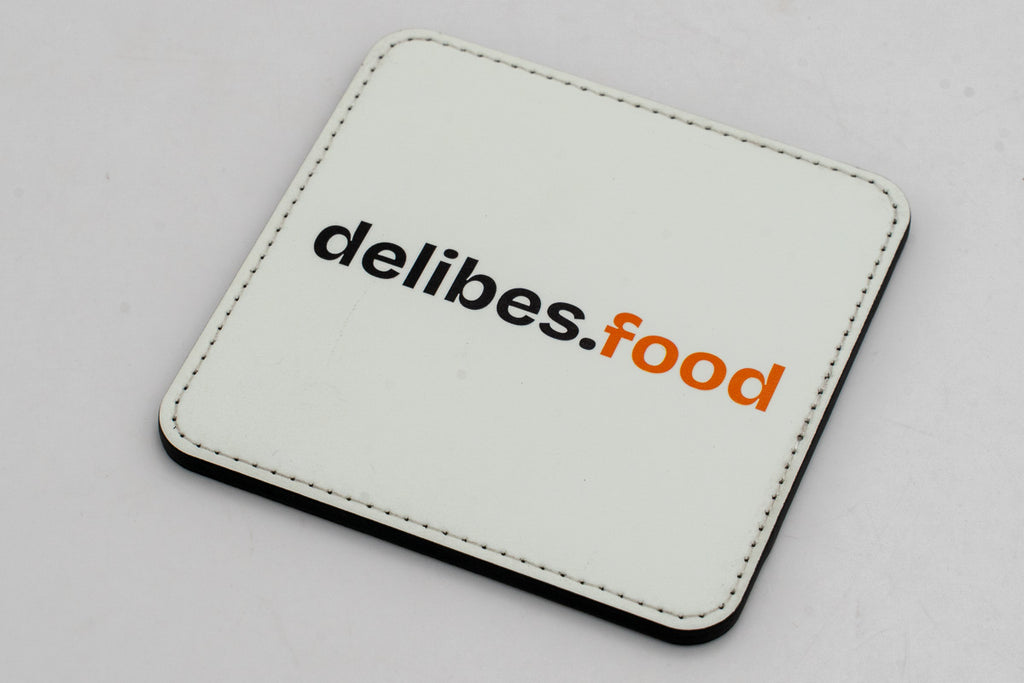 Square white coaster with a black and orange delibes.Food logo.