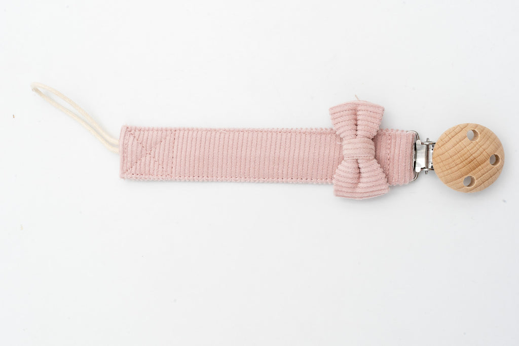 Pink dummy clip with a bow beside the round wooden clip