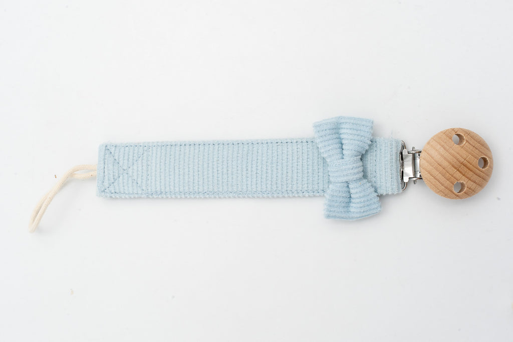 Light blue dummy clip with a bow beside the round wooden clip