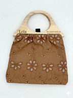 Bolso de tela marrón con asa de madera grabada Lola y patrón calado de flores.