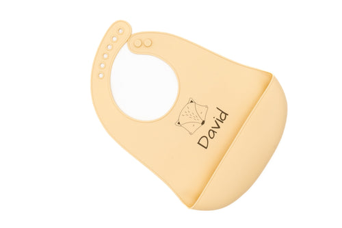 Beige silicone bib with a name and geometric animal motif, viewed diagonally.