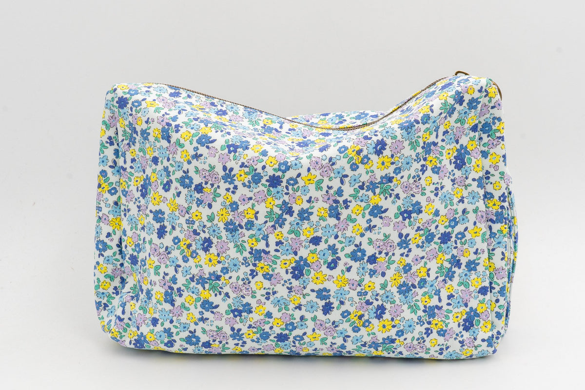 Fabric toiletry bag with blue and yellow flowers, front view on a neutral background