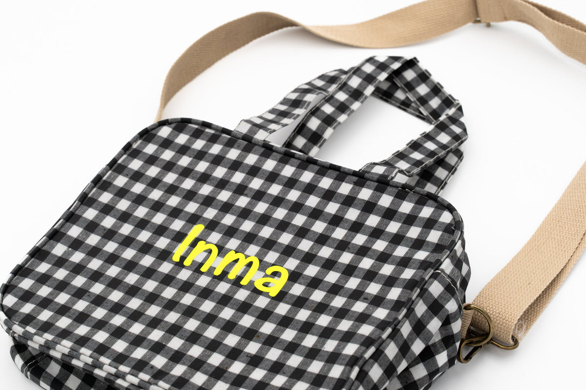 Black gingham change bag with the name Inma in yellow vinyl and shoulder strap
