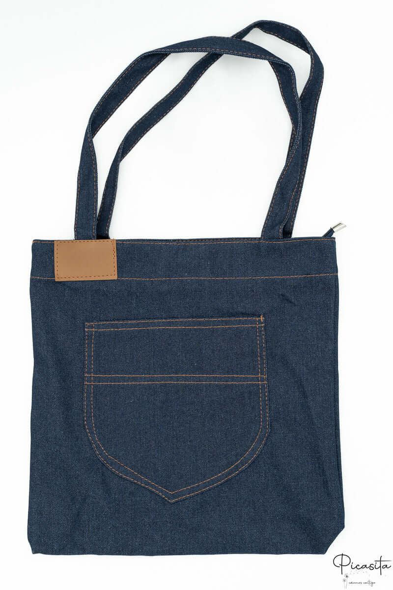 Vista trasera de bolso vaquero con bolsillo grande y parche rectangular de polipiel marrón.