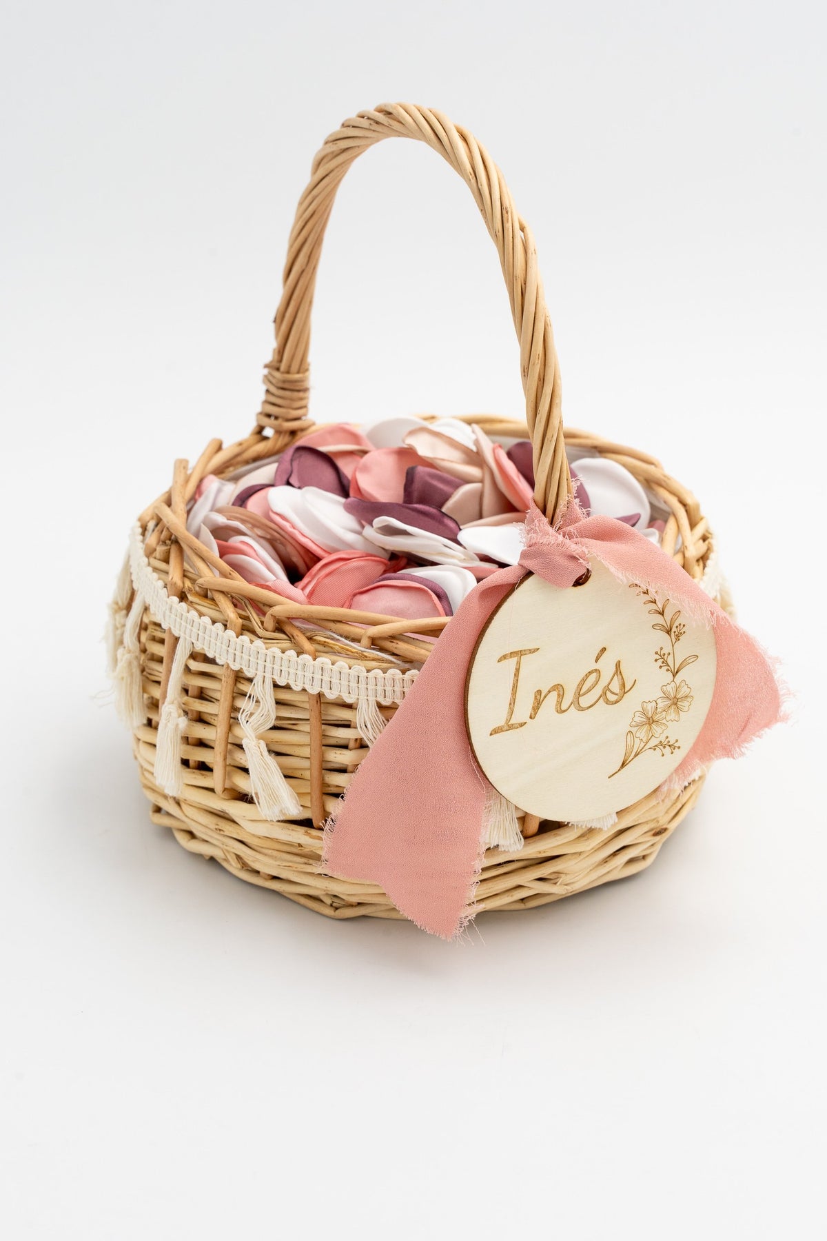 Cesta de ratán con lazo de gasa rosa y etiqueta de madera con nombre grabado.
