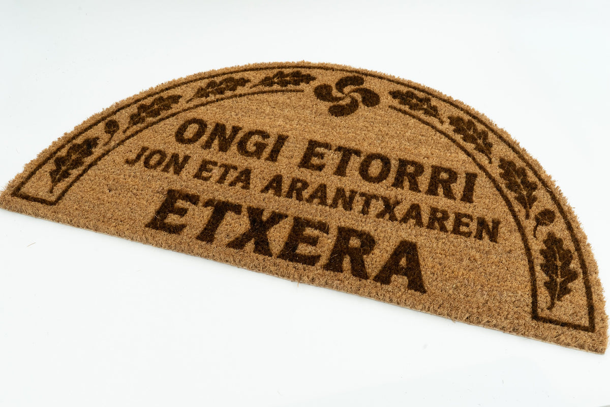 Felpudo en euskera semicircular con texto Ongi Etorri y motivos de hojas de roble.