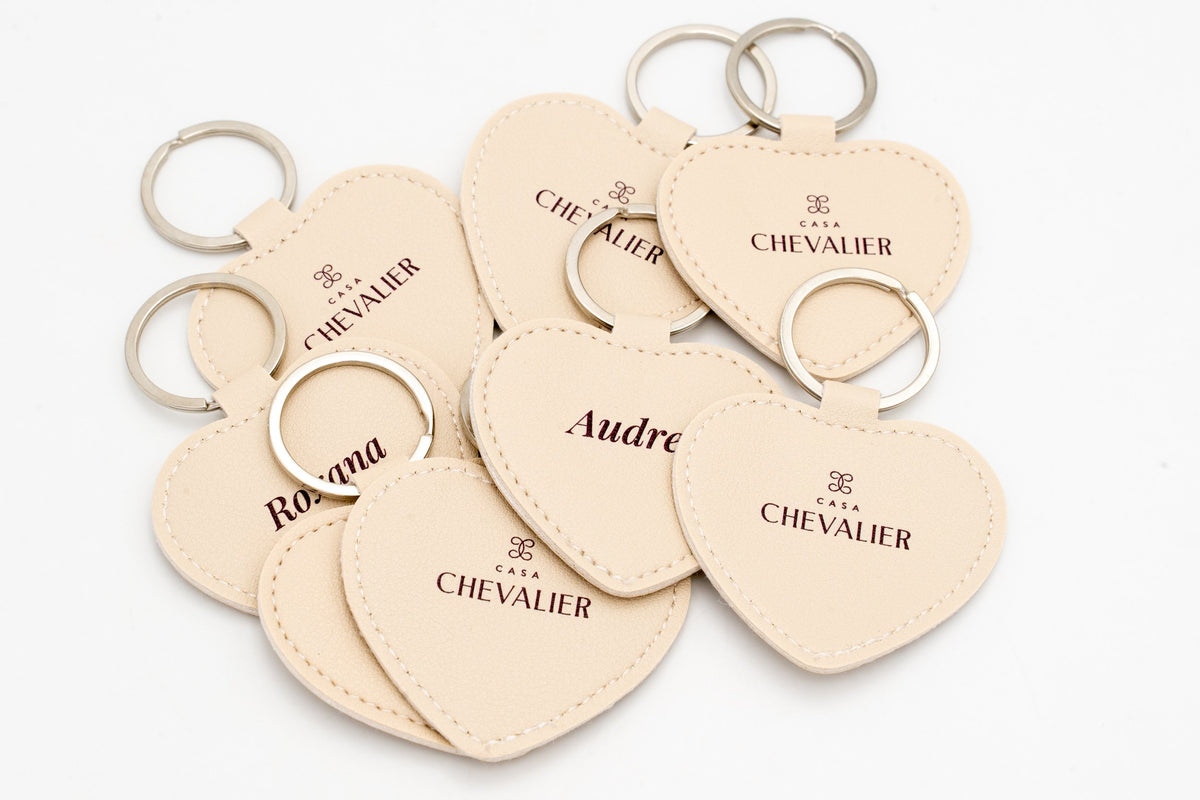 Beige heart keyrings with names and dark logos, without bows in the image.