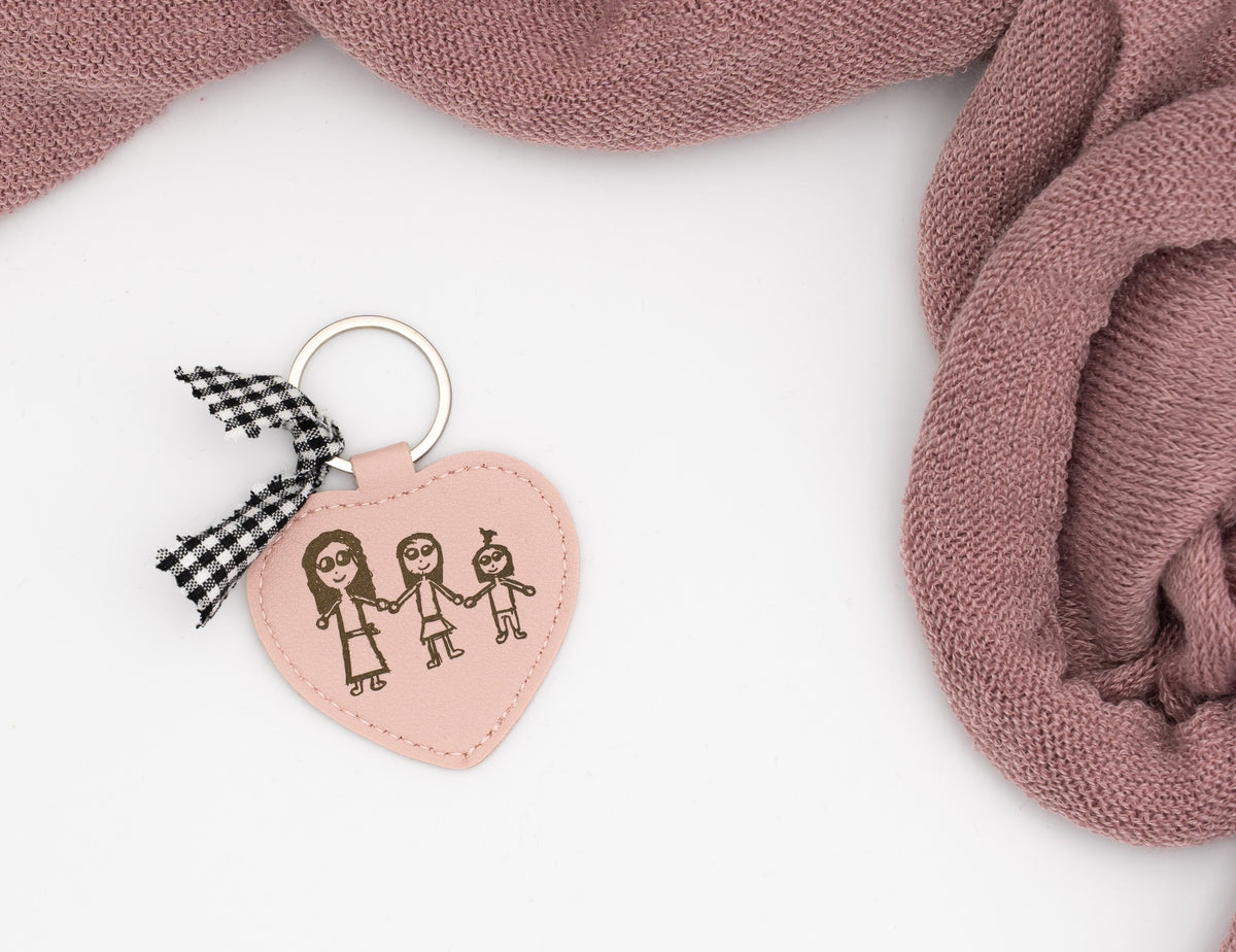 Pink heart keyring with a drawing of three people and a black gingham bow.