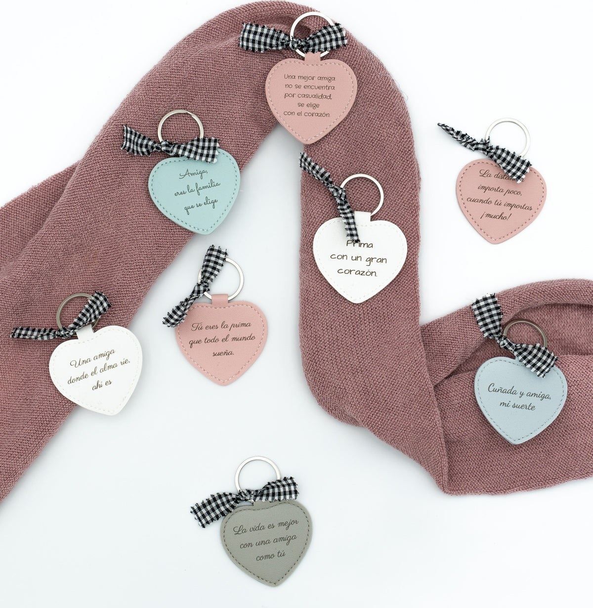 Arrangement of heart keyrings with messages and bows on pink fabric.