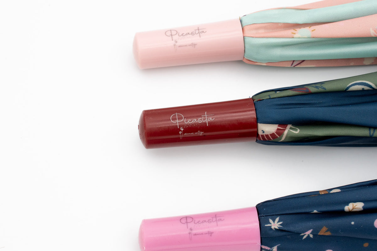 Three closed children's umbrellas with a name printed on the light pink, burgundy and pink handles