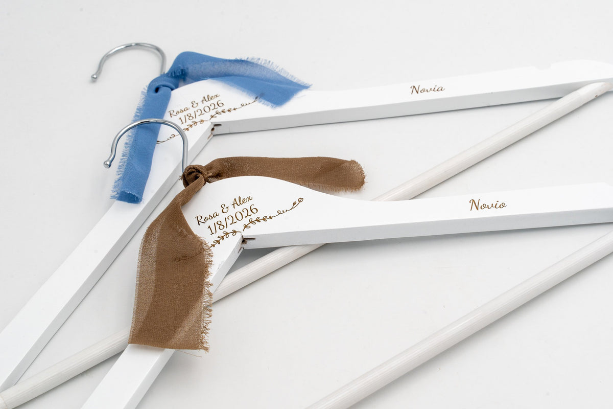 Two white hangers for the bride and groom with names and date engraved and blue and brown chiffon bows