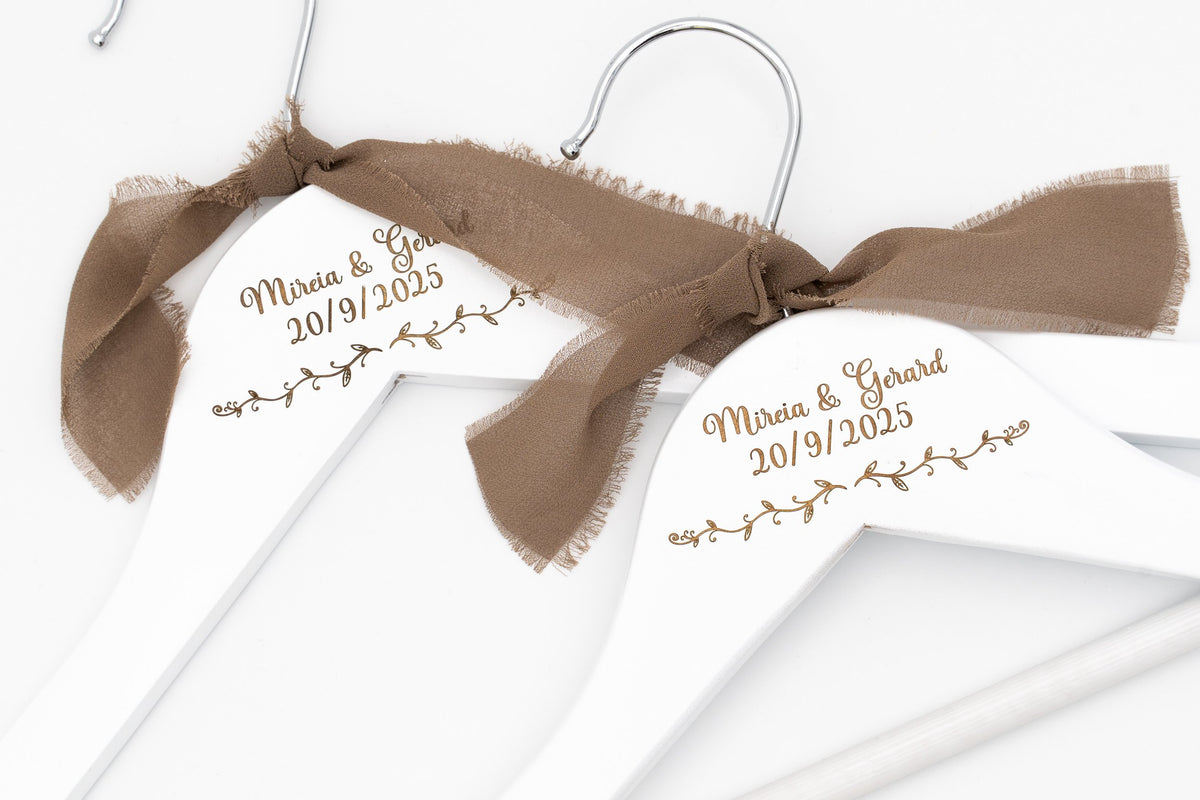 Two white hangers with the names Miria and Gerard and the date 20/9/2025 engraved, with brown bows
