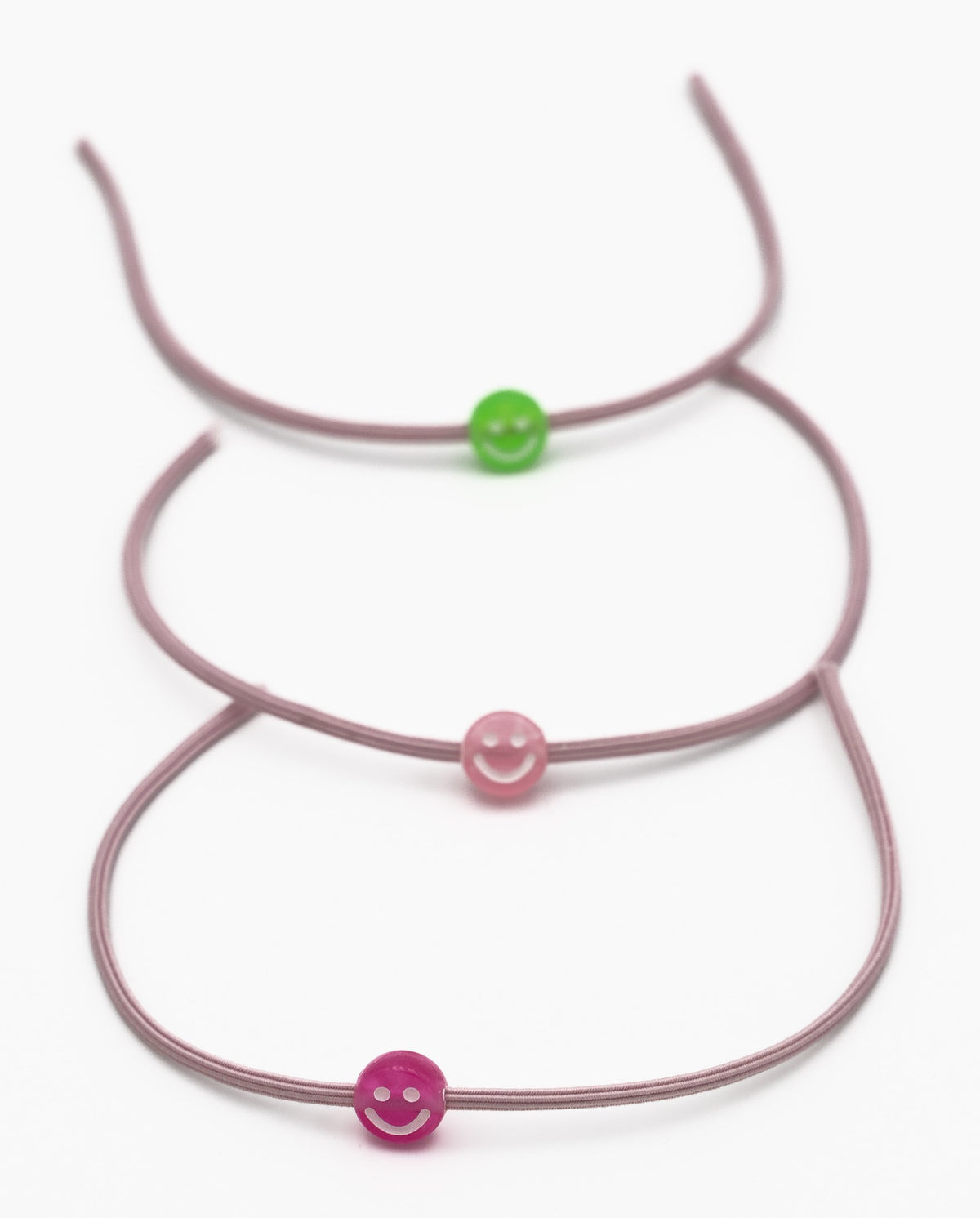 Three elastic mauve bracelets with green and pink smile-shaped silicone beads