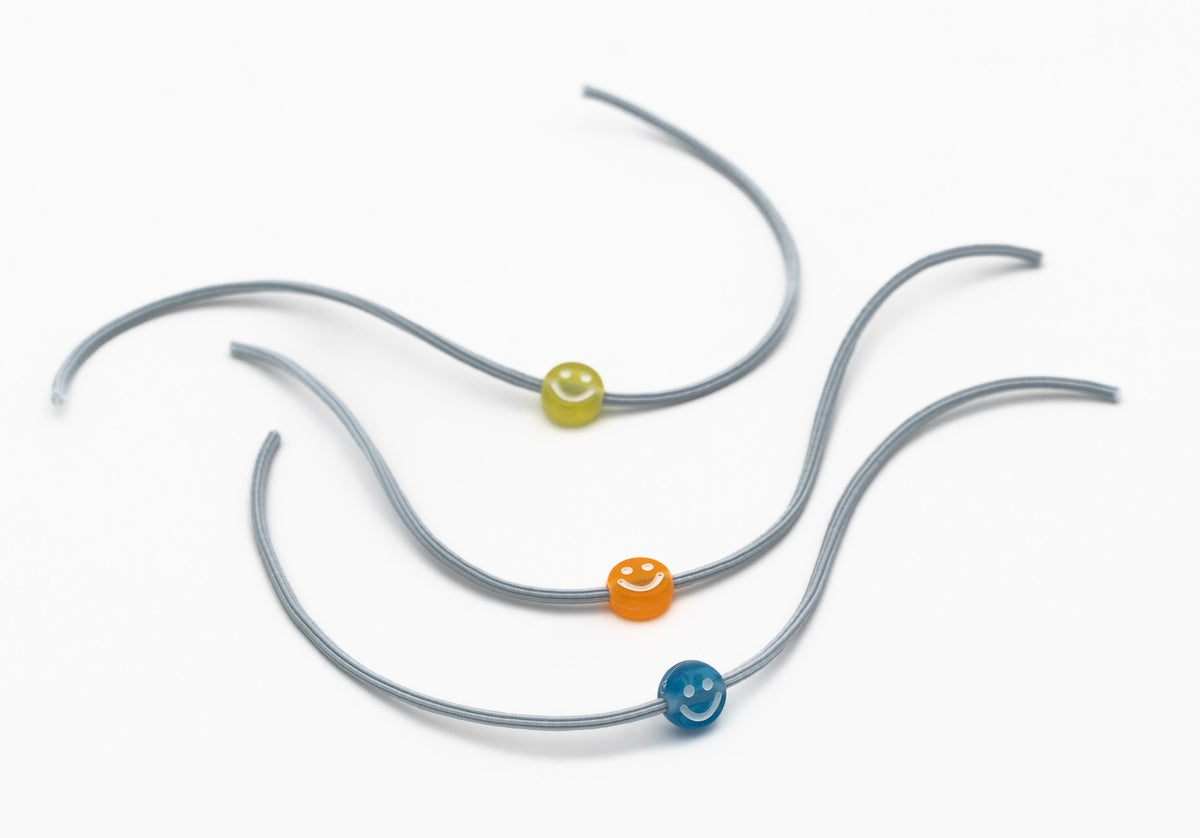 Detalle de pulseras infantiles con cuentas de silicona de caritas sonrientes sobre cordón elástico gris.