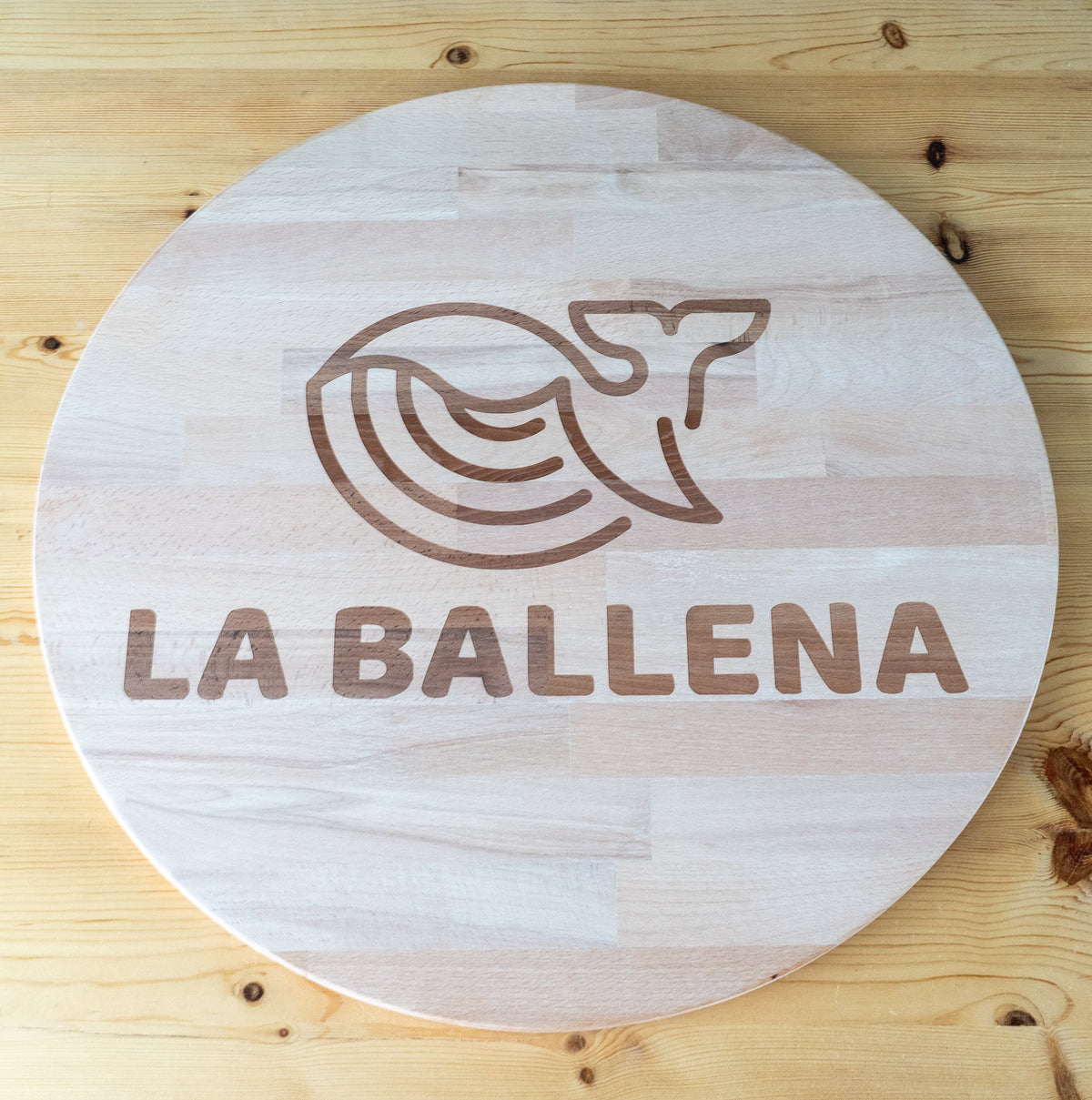 Tablero redondo de madera con una ballena y el nombre La Ballena grabados.