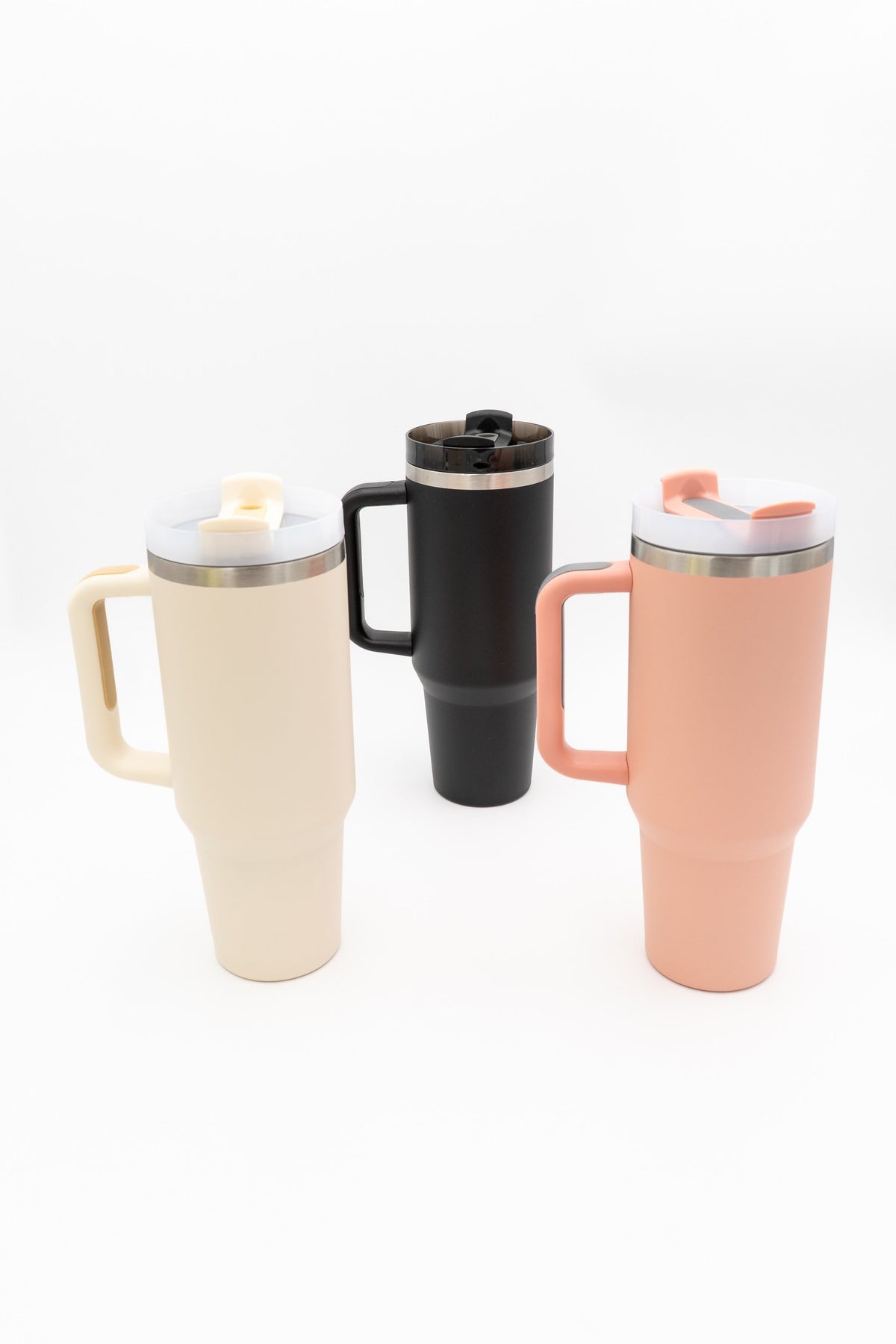 Three handled travel tumblers in cream, black and salmon on a white background