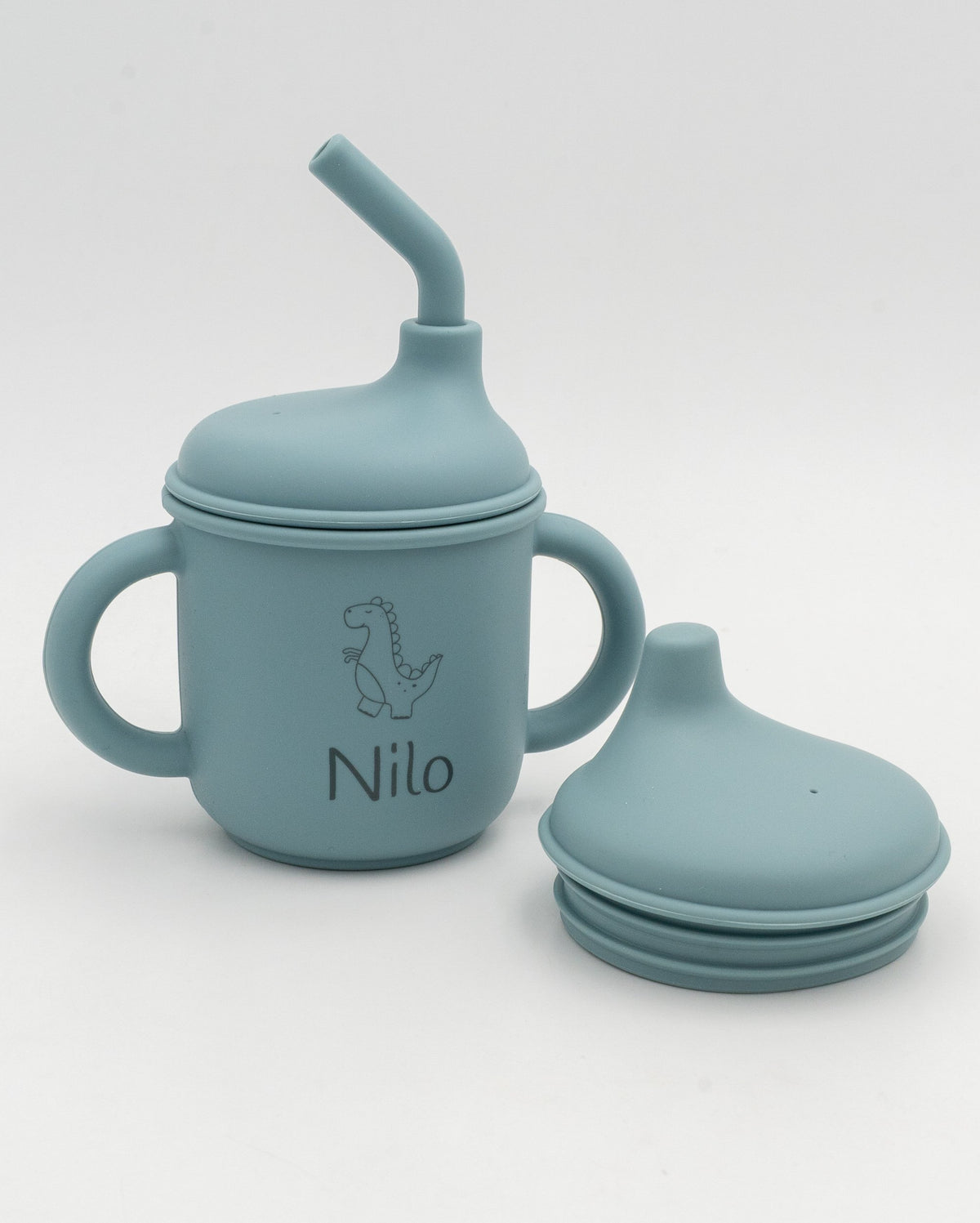 Greyish-blue 3-in-1 cup with the name Nilo and a dinosaur engraved, next to the sippy lid